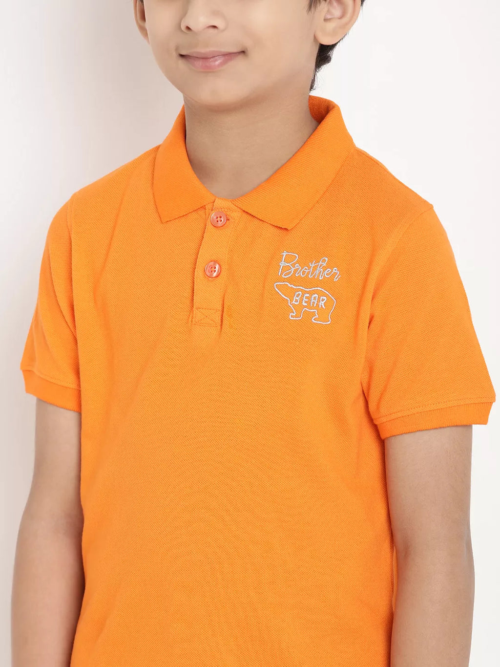 Child wearing an orange polo shirt with a logo on a plain background