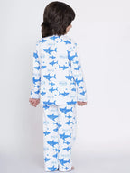 Child wearing a white pajama set with blue shark prints on a plain background