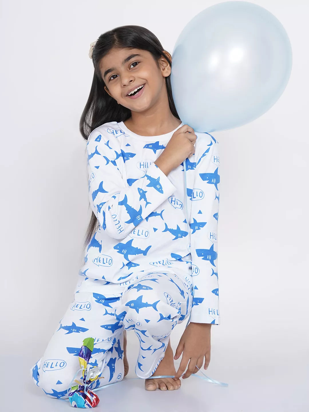 Child wearing shark-patterned pajamas holding a blue balloon against a white background