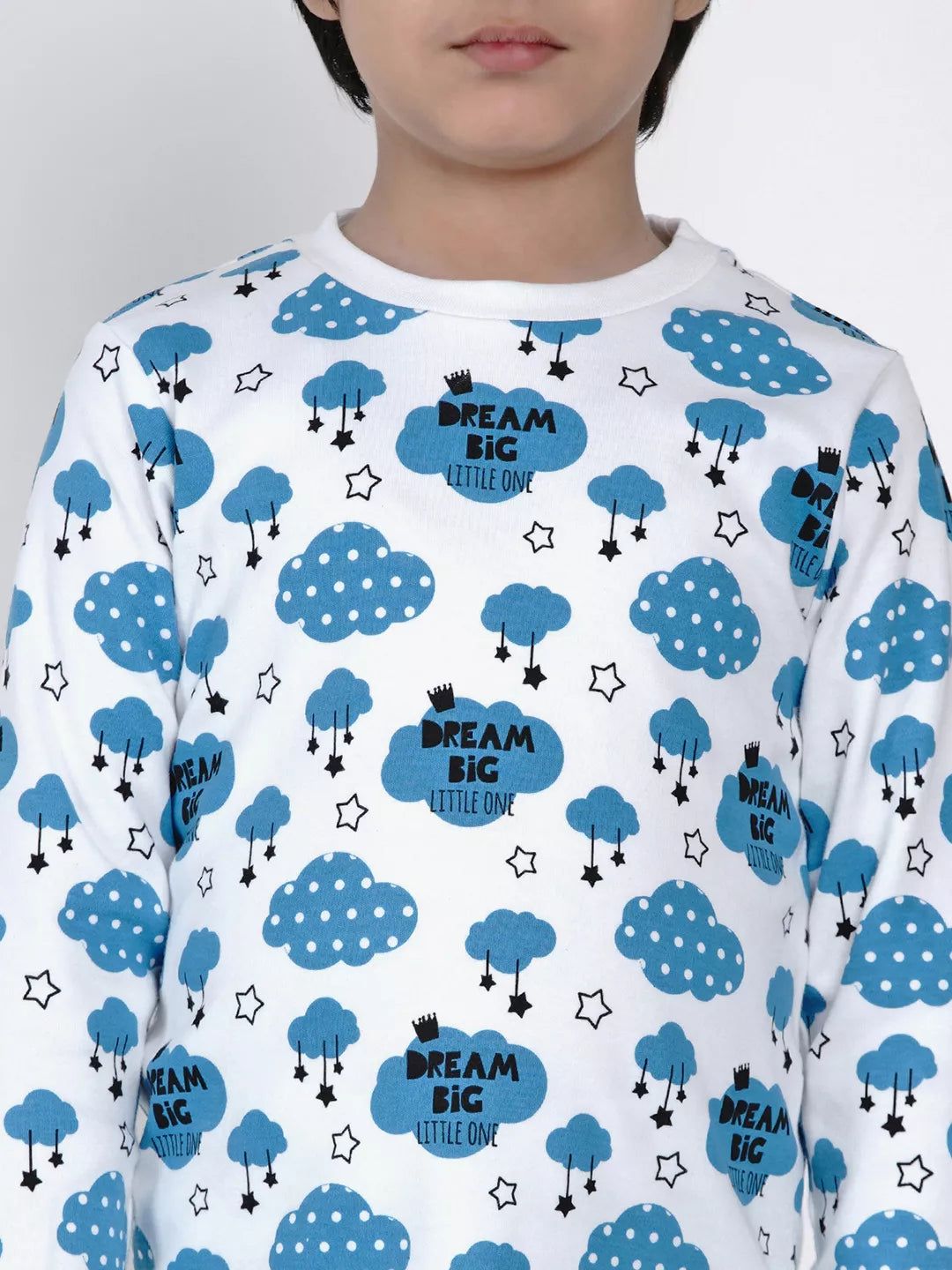 Child wearing a white shirt with blue cloud patterns and 'Dream Big Little One' text.