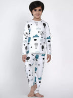 Child wearing a white pajama set with cloud and animal patterns on a plain background