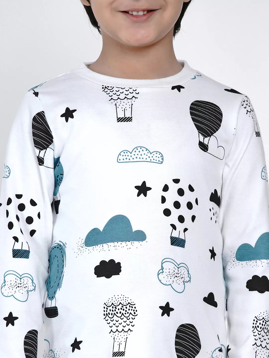 Child wearing a white long-sleeve shirt with black, blue, and gray cloud and sheep pattern on a plain background