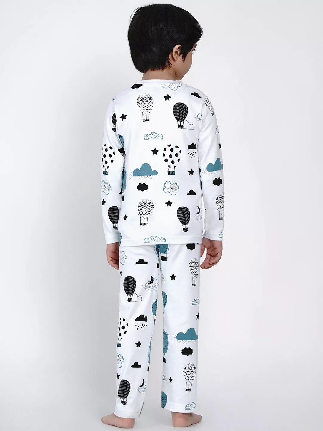 Child wearing a white pajama set with black and blue cloud, star, and hot air balloon patterns on a white background.