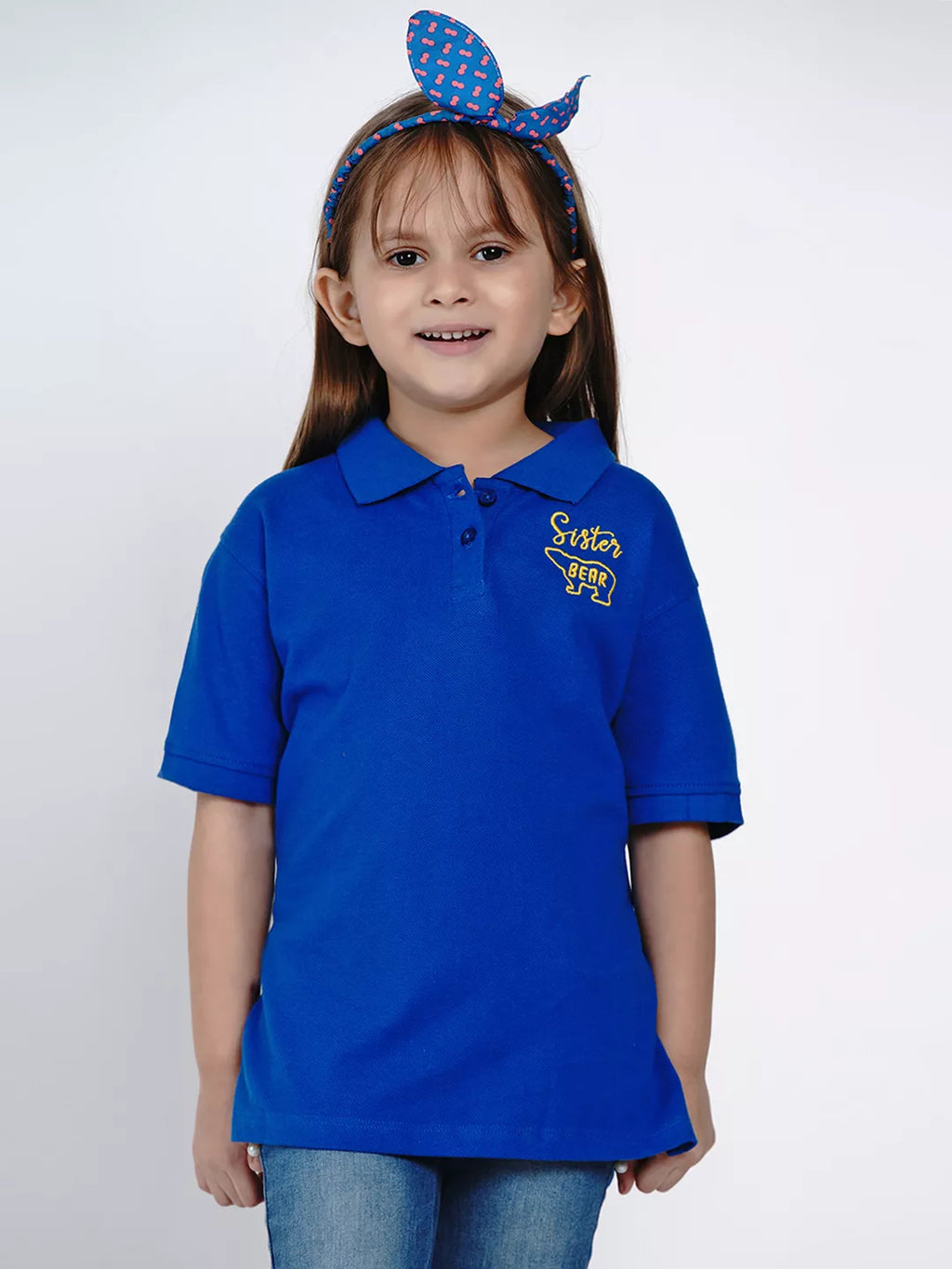 Young girl wearing a blue polo shirt with 'Sister' printed on it, against a white background