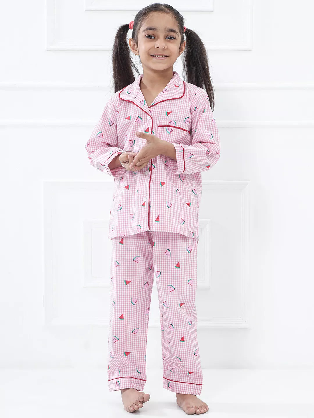 Young girl wearing a pink checkered pajama set with heart patterns on a white background