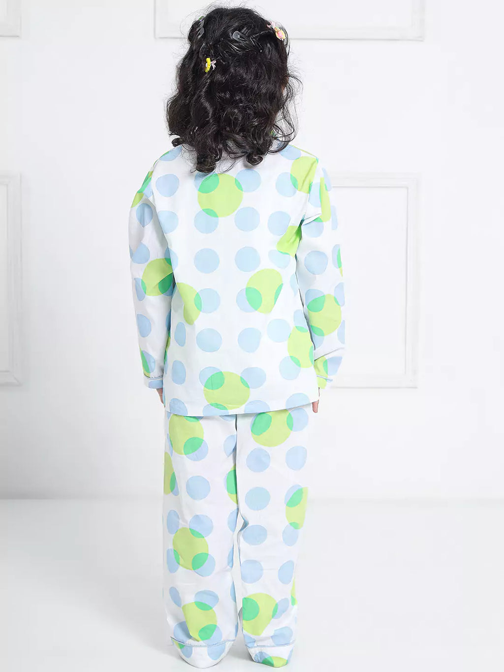 Child wearing a polka dot pajama set with green, blue, and white pattern on a white background