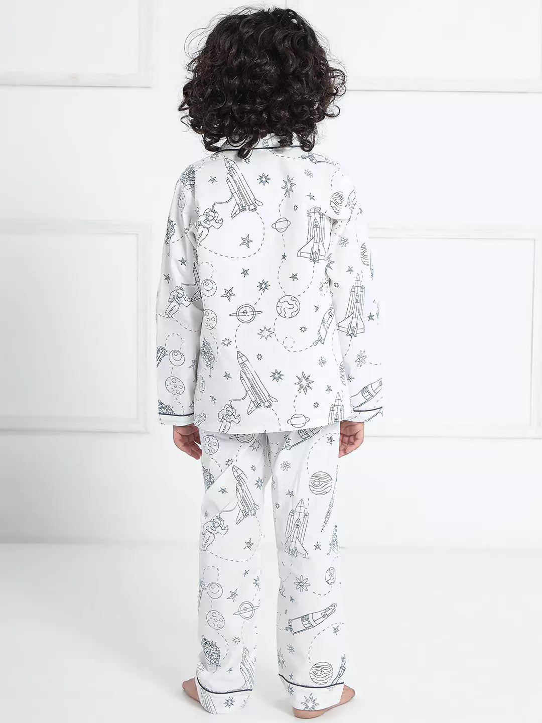 Child wearing a white pajama set with space-themed design on a white background
